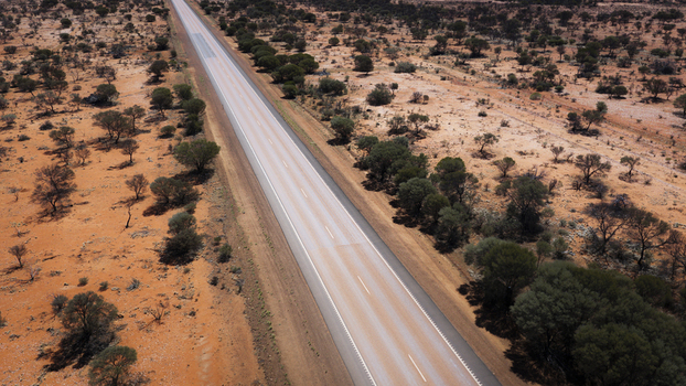 Aerial view of a long straight asphalt road stretching through the arid red landscape of the Australian outback with sparse trees and shrubs in Perth Western Australia Australia.