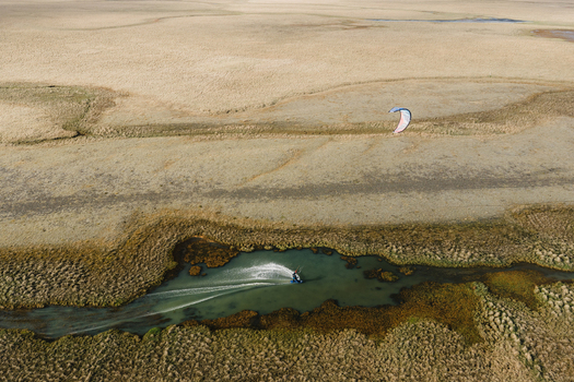 Aerial view of a kiteboarder gliding through a narrow winding stream amidst vast grassy plains in Hofn Sveitarfelagid Hornaf Iceland.