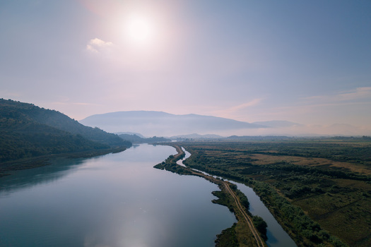 Aerial view of the winding Kanali i Vivarit waterway flowing through lush wetlands and rolling hills under a bright hazy sun in Vrine Vlore County Albania. Aerial view of the winding Kanali i Vivarit waterway flowing through lush wetlands and rolling hills under a bright hazy sun in Vrine Vlore County Albania.