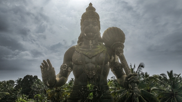 Aerial view of the large Hanuman statue holding a mace set against a dramatic cloudy sky and lush palm trees in Udupi Karnataka India. Aerial view of the large Hanuman statue holding a mace set against a dramatic cloudy sky and lush palm trees in Udupi Karnataka India.