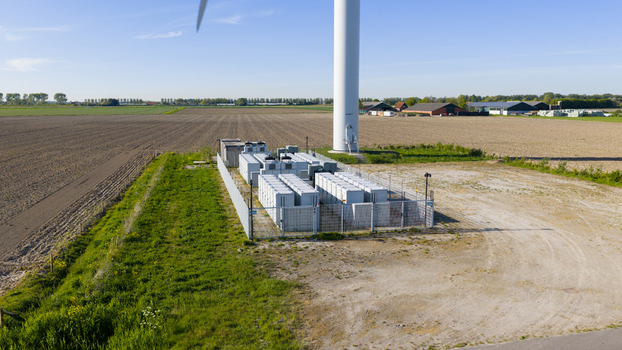 Aerial view of a large battery energy storage system in a fenced enclosure at the base of a wind turbine in a rural landscape Ooltgensplaat South Holland Netherlands. Aerial view of a large battery energy storage system in a fenced enclosure at the base of a wind turbine in a rural landscape Ooltgensplaat South Holland Netherlands.