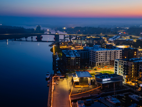 Aerial view of Riverfront Park at twilight with illuminated buildings a bridge spanning the Cape Fear River and boats docked at the marina in Wilmington North Carolina United States.