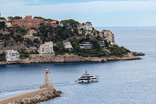 Aerial view of a luxury yacht passing the lighthouse at the entrance of the port with coastal hillside villas in the background in Nice Provence Alpes Cote d Azur France. Aerial view of a luxury yacht passing the lighthouse at the entrance of the port with coastal hillside villas in the background in Nice Provence Alpes Cote d Azur France.
