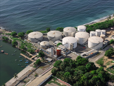 Aerial view of industrial storage tanks situated along the coastline with small boats docked in the harbor in Bajos de Haina San Cristobal Provinc Dominican Republic.
