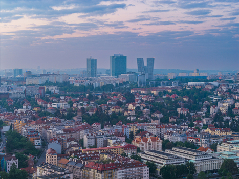 Aerial view of the Prague skyline featuring modern skyscrapers like the V Tower and City Tower rising above historic residential rooftops and lush green trees in Prague Prague Czechia.