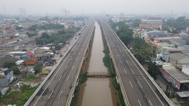 Aerial view of the elevated toll road stretching over a canal flanked by dense urban residential areas and lush greenery in Bekasi Barat West Java Indonesia. Aerial view of the elevated toll road stretching over a canal flanked by dense urban residential areas and lush greenery in Bekasi Barat West Java Indonesia.