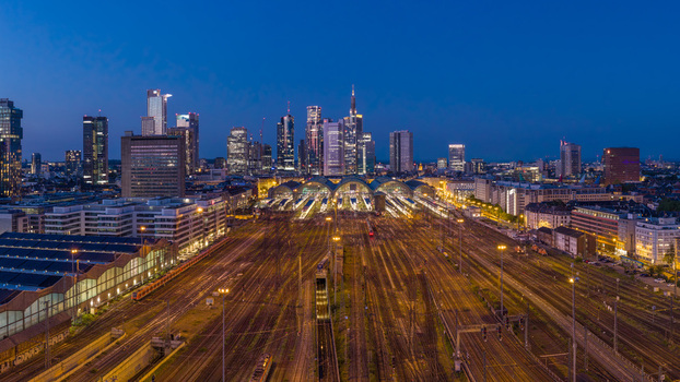 Aerial view of the Hauptbahnhof train station and illuminated railway tracks with the city skyline in the background at twilight in Frankfurt am Main Hessen Germany.