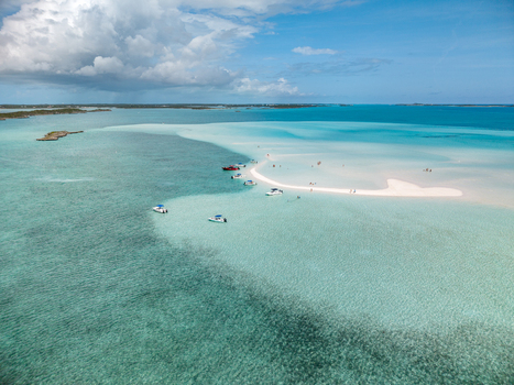 Aerial view of the Man O War Cay Sandbar with boats anchored in crystal clear turquoise water and people relaxing on the white sand under a cloudy sky in Rolletown Exuma The Bahamas. Aerial view of the Man O War Cay Sandbar with boats anchored in crystal clear turquoise water and people relaxing on the white sand under a cloudy sky in Rolletown Exuma The Bahamas.