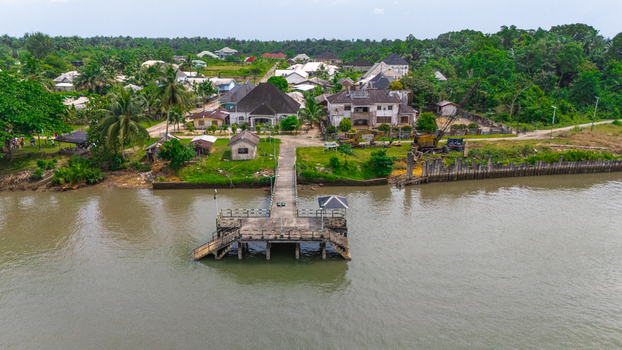 Aerial view of a concrete pier extending into a river surrounded by lush tropical vegetation and residential houses in Minima Rivers Nigeria.