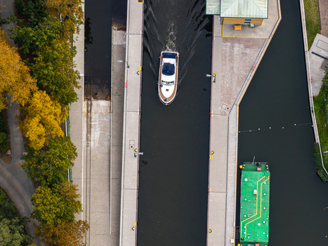 Aerial view of Schleuse Spandau with a motorboat navigating the lock chamber alongside a green barge surrounded by autumn trees in Berlin Berlin Germany.