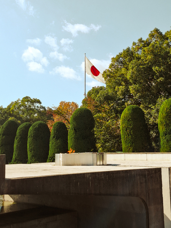 View of the Peace Flame at the Hiroshima Peace Memorial Park with the Japanese flag flying in the background and manicured hedges in Hiroshima Hiroshima Japan. View of the Peace Flame at the Hiroshima Peace Memorial Park with the Japanese flag flying in the background and manicured hedges in Hiroshima Hiroshima Japan.
