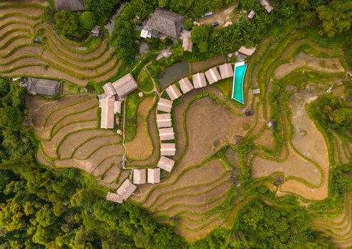 Aerial view of terraced rice fields and a resort with bungalows and a swimming pool nestled in the lush mountains of Hoang Su Phi Ha Giang Vietnam.