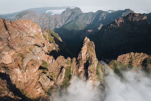 Aerial view of jagged peaks pierce through soft blankets of clouds textured rock formations and shadowed valleys Pico do Areeiro Madeira Portugal.