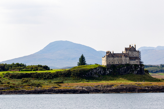 View of Duart Castle standing on a rocky cliff overlooking the sea with rolling hills and mountains in the background Isle of Mull Scotland United Kingdom.