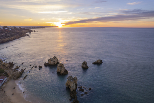 Aerial view of Praia dos Arrifes with dramatic rock formations rising from the calm sea at sunset along the coastline of the Faro District Portugal. Aerial view of Praia dos Arrifes with dramatic rock formations rising from the calm sea at sunset along the coastline of the Faro District Portugal.
