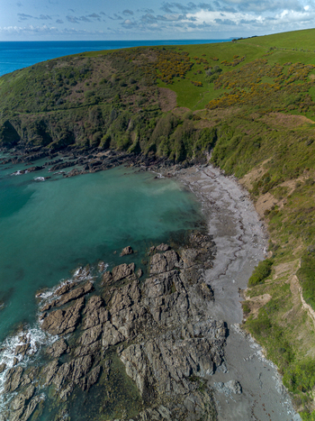 Aerial view of Portnadler Bay featuring rugged rocky coastline turquoise waters and lush green grassy cliffs under a clear sky in Looe Cornwall United Kingdom. Aerial view of Portnadler Bay featuring rugged rocky coastline turquoise waters and lush green grassy cliffs under a clear sky in Looe Cornwall United Kingdom.