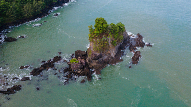 Aerial view of Karang Agung Beach featuring a massive rock formation with green trees surrounded by the sea in Ayah Central Java Indonesia. Aerial view of Karang Agung Beach featuring a massive rock formation with green trees surrounded by the sea in Ayah Central Java Indonesia.