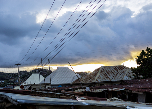 View of rooftops with metal sheets and power lines under a dramatic cloudy sky at sunset in Jos Plateau Nigeria. View of rooftops with metal sheets and power lines under a dramatic cloudy sky at sunset in Jos Plateau Nigeria.
