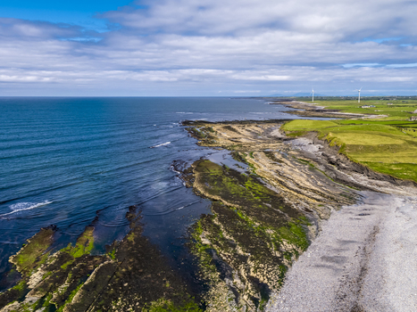 Aerial view of Storm Beach featuring rugged rocky coastline vibrant green fields and distant wind turbines along the Atlantic coast in Carrownedin County Sligo Ireland.