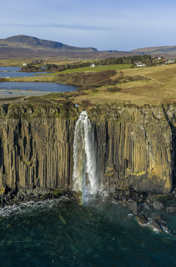 Aerial view of Kilt Rock and Mealt Falls cascading down basalt cliffs into the sea with a rainbow at the base under a clear sky in Isle of Skye Scotland United Kingdom. Aerial view of Kilt Rock and Mealt Falls cascading down basalt cliffs into the sea with a rainbow at the base under a clear sky in Isle of Skye Scotland United Kingdom.
