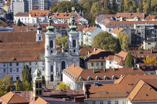 View of sun drenched terracotta rooftops meet the sky punctuated by the baroque elegance of a church under a blue sky Graz Styria Austria. View of sun drenched terracotta rooftops meet the sky punctuated by the baroque elegance of a church under a blue sky Graz Styria Austria.