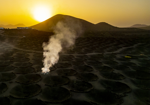 Aerial view of volcanic landscape with smoke rising from a vent at sunset in Lanzarote Canarias Spain. Aerial view of volcanic landscape with smoke rising from a vent at sunset in Lanzarote Canarias Spain.