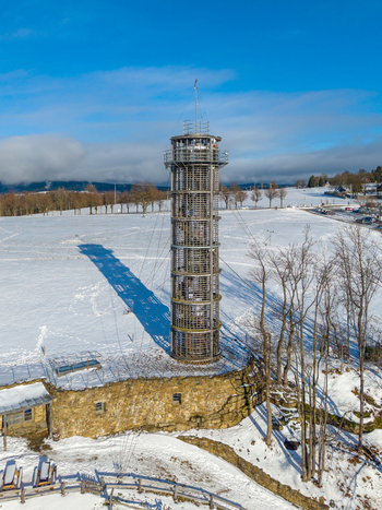 Aerial view of Majak Jary Cimrmana observation tower standing in a snow covered landscape with bare trees and clear blue sky in Korenov Liberecky kraj Czechia. Aerial view of Majak Jary Cimrmana observation tower standing in a snow covered landscape with bare trees and clear blue sky in Korenov Liberecky kraj Czechia.