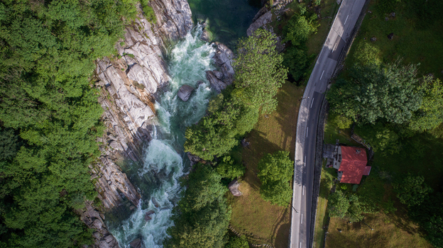 Aerial view of Valle Verzasca with rushing white water rapids rocky banks and a road winding through lush green forest in Verzasca Ticino Switzerland. Aerial view of Valle Verzasca with rushing white water rapids rocky banks and a road winding through lush green forest in Verzasca Ticino Switzerland.