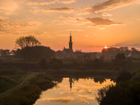 Aerial view of the historic town silhouette with the prominent church tower reflected in the calm water during a golden sunset Veere Zeeland Netherlands.