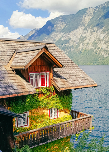 View of a traditional wooden house with ivy covered walls and red window frames overlooking the serene Hallstatt lake with mountains in the background in Hallstatt Upper Austria Austria. View of a traditional wooden house with ivy covered walls and red window frames overlooking the serene Hallstatt lake with mountains in the background in Hallstatt Upper Austria Austria.