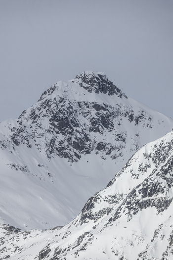 View of a snow covered mountain peak with jagged rocky ridges under an overcast winter sky in the Arctic landscape Ersfjord Troms Norway. View of a snow covered mountain peak with jagged rocky ridges under an overcast winter sky in the Arctic landscape Ersfjord Troms Norway.