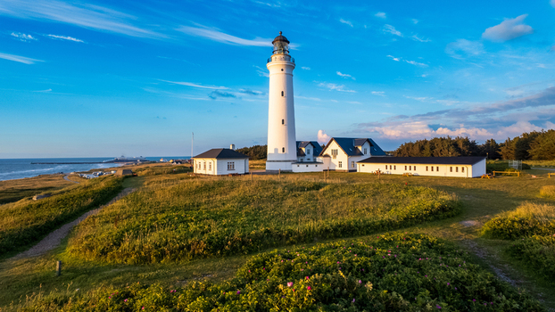 Aerial view of Hirtshals Lighthouse standing on green dunes under a blue sky with wispy clouds at sunset in Hirtshals Denmark.