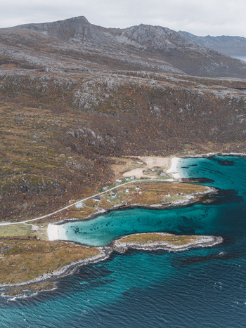 Aerial view of Senja island coastline featuring turquoise waters rocky cliffs and small coastal houses nestled along the winding road in Senja Troms Norway.