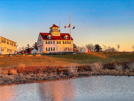 View of the US Coast Guard Station Martha s Vineyard with its distinctive red roof and white facade during golden hour across a calm pond in Edgartown Massachusetts United States.