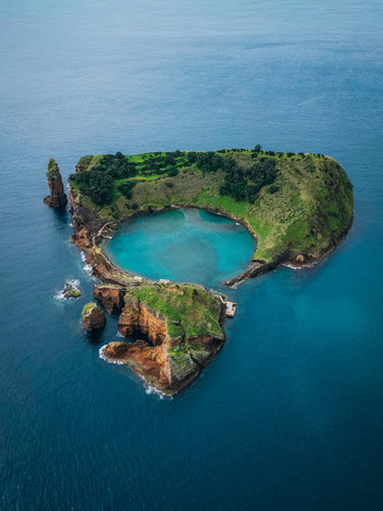 Aerial view of the lush green islet with a stunning turquoise crater lake contrasts sharply against the deep blue sea Vila Franca do Campo Portugal.