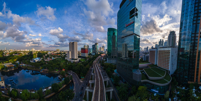 South Jakarta Indonesia 10 January 2026 Aerial view of modern skyscrapers an elevated railway track and lush greenery under a blue sky with scattered clouds. South Jakarta Indonesia 10 January 2026 Aerial view of modern skyscrapers an elevated railway track and lush greenery under a blue sky with scattered clouds.