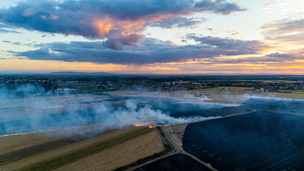 Aerial view of a field fire burning in agricultural land with thick smoke rising under a dramatic sunset sky in Sremska Mitrovica Vojvodina Serbia. Aerial view of a field fire burning in agricultural land with thick smoke rising under a dramatic sunset sky in Sremska Mitrovica Vojvodina Serbia.