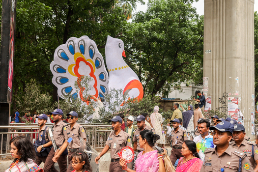 Dhaka Bangladesh 13 April 2026 View of a vibrant festive procession with towering colorful peacock and dove floats amidst a bustling crowd and lush greenery.