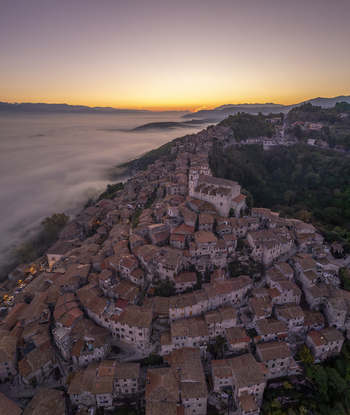 Aerial view of the historic hilltop town of Artena with its dense stone buildings and terracotta rooftops emerging above a sea of morning fog in Artena Lazio Italy.