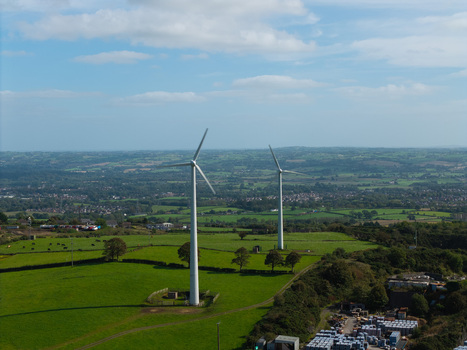 Aerial view of wind turbines in a green landscape with scattered trees and a storage area in the foreground in Lisburn Northern Ireland United Kingdom. Aerial view of wind turbines in a green landscape with scattered trees and a storage area in the foreground in Lisburn Northern Ireland United Kingdom.