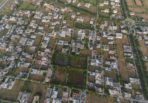 Aerial view of a residential neighborhood with a grid street layout houses with flat roofs solar panels and open plots in Lahore Punjab Pakistan.