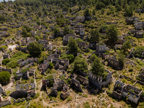 Aerial view of the historic ghost village of Kayakoy formerly known as Levissi featuring abandoned stone houses ruins and lush greenery on a hillside in Fethiye Mugla Turkiye. Aerial view of the historic ghost village of Kayakoy formerly known as Levissi featuring abandoned stone houses ruins and lush greenery on a hillside in Fethiye Mugla Turkiye.