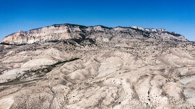 Aerial view of the rugged mountain landscape with rocky terrain and sparse vegetation under a clear blue sky near Cody Wyoming United States.