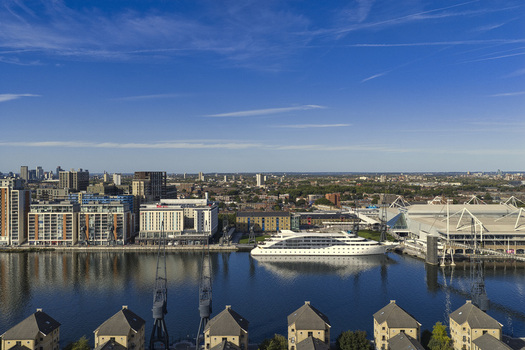 Aerial view of ExCeL London exhibition centre and a cruise ship docked at the Royal Docks with modern buildings and industrial cranes under a clear blue sky in London England United Kingdom.