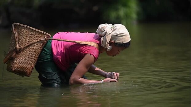 View of a woman with a basket washing in a river Bangladesh.