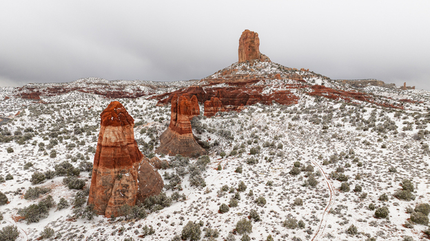 Aerial view of snow covered red rock buttes and sandstone formations rising from a desert landscape under an overcast sky in Page Arizona United States.