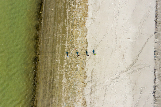 Aerial view of people walking along the sandy shoreline of Kuakata beach with calm water and footprints in the sand in Kuakata Barisal Division Bangladesh. Aerial view of people walking along the sandy shoreline of Kuakata beach with calm water and footprints in the sand in Kuakata Barisal Division Bangladesh.