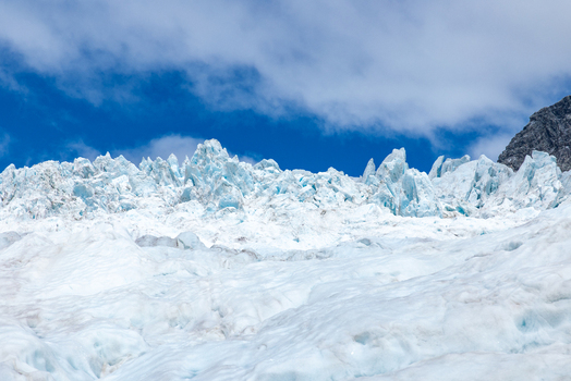 View of the glacier s icy expanse under a blue sky with scattered clouds creating a striking contrast Franz Josef Glacier West Coast Region New Zealand. View of the glacier s icy expanse under a blue sky with scattered clouds creating a striking contrast Franz Josef Glacier West Coast Region New Zealand.
