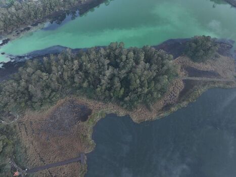 Aerial view of volcanic Dieng Plateau featuring the vibrant green waters of Telaga Warna lake surrounded by dense forest and a wooden boardwalk in Kejajar Central Java Indonesia. Aerial view of volcanic Dieng Plateau featuring the vibrant green waters of Telaga Warna lake surrounded by dense forest and a wooden boardwalk in Kejajar Central Java Indonesia.