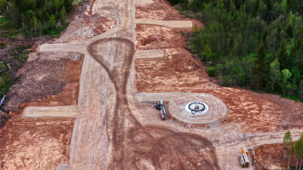 Aerial view of a wind turbine foundation under construction with circular concrete base and dirt access roads surrounded by forest in Latvia. Aerial view of a wind turbine foundation under construction with circular concrete base and dirt access roads surrounded by forest in Latvia.